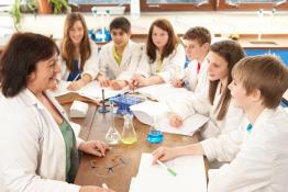 Adult and teenagers in lab coats smiling
