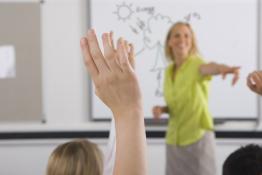 A confident looking teacher is surrounded by a sea of hands up from the class